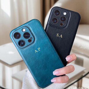 May include: Two phone cases, one teal blue and one black, with a leather texture. Both cases have a gold monogram, one says "A.P." and the other says "S.A."