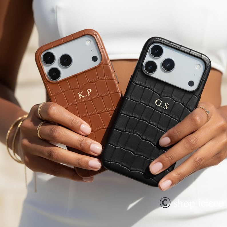 Puede incluir: Se muestran dos fundas para tel&eacute;fono, una marr&oacute;n y otra negra. Ambas fundas tienen una textura de piel de cocodrilo e iniciales doradas. La funda marr&oacute;n tiene las iniciales "K.P" y la funda negra "G.S".
