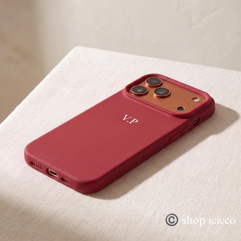 May include: A deep red smartphone case featuring a metallic copper-toned camera module and the white monogram initials V.P. printed on the back. The case includes precise cutouts for the camera lenses, flash, charging port, and side buttons.