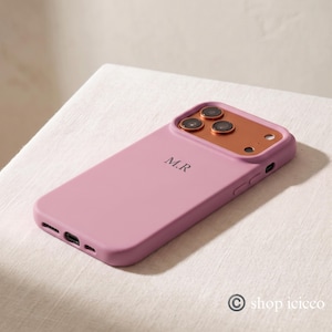 May include: A matte mauve phone case featuring the initials M.R in a dark serif font. The case includes a metallic copper-toned camera housing with three circular lens cutouts and a small circular flash opening on the upper right side.