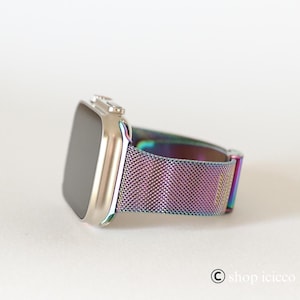 K&ouml;nnte beinhalten: Eine silberne Smartwatch mit rechteckigem Bildschirm und einem metallisch schillernden Mesh-Armband. Das Armband wechselt durch Farbt&ouml;ne von Lila, Blau und Gr&uuml;n. Die Uhr wird auf einer wei&szlig;en Oberfl&auml;che gezeigt.