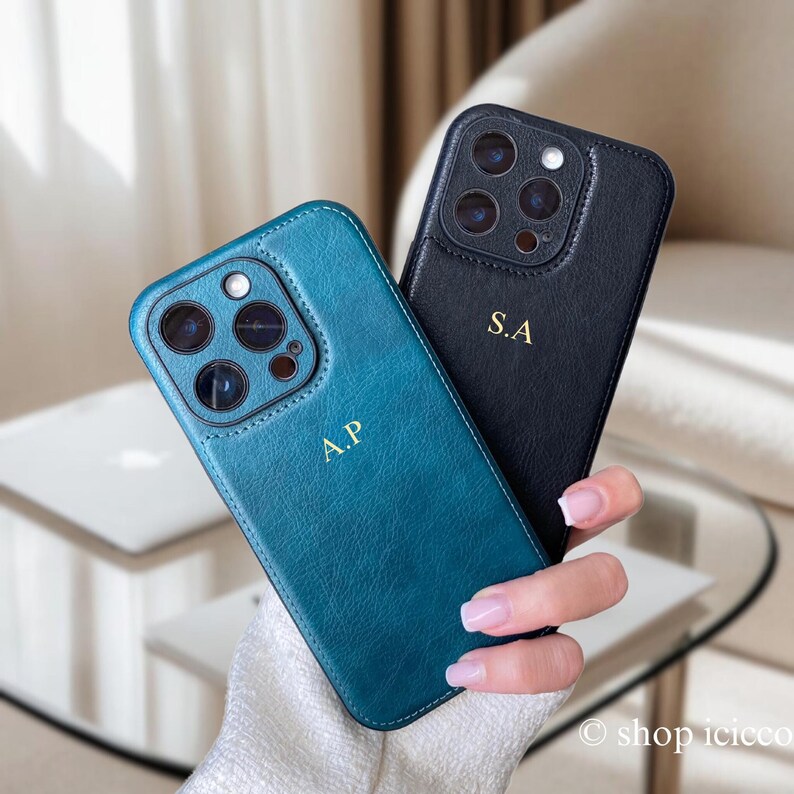 May include: Two phone cases, one teal blue and one black, with a leather texture. Both cases have a gold monogram, one says "A.P." and the other says "S.A."