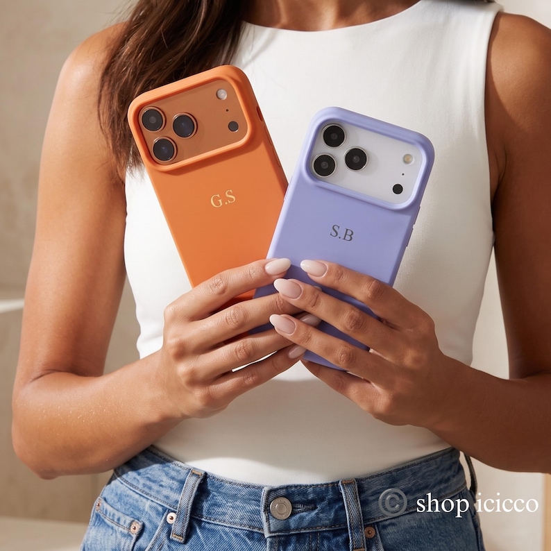May include: Two smartphone cases, one orange and one lavender, each featuring a triple camera cutout and gold-toned lettering. The orange case is personalized with the initials G.S, while the lavender case is personalized with the initials S.B.