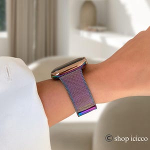 K&ouml;nnte beinhalten: Eine ros&eacute;goldene Smartwatch mit einem Regenbogen-Mesh-Armband wird am Handgelenk getragen. Das Uhrengeh&auml;use hat eine abgerundete rechteckige Form. Das Armband besteht aus feinem, gewebtem Metall, das mehrere Farben reflektiert. Die Uhr wird mit einem Magnetverschluss befestigt.
