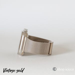 K&ouml;nnte beinhalten: Eine silberfarbene Smartwatch mit einem Mesh-Armband. Das Zifferblatt der Uhr ist rechteckig mit abgerundeter Kante. Das Armband besteht aus feinem, gewebtem Metall. Die Worte "Vintage gold" sind unten links in Schreibschrift gedruckt.