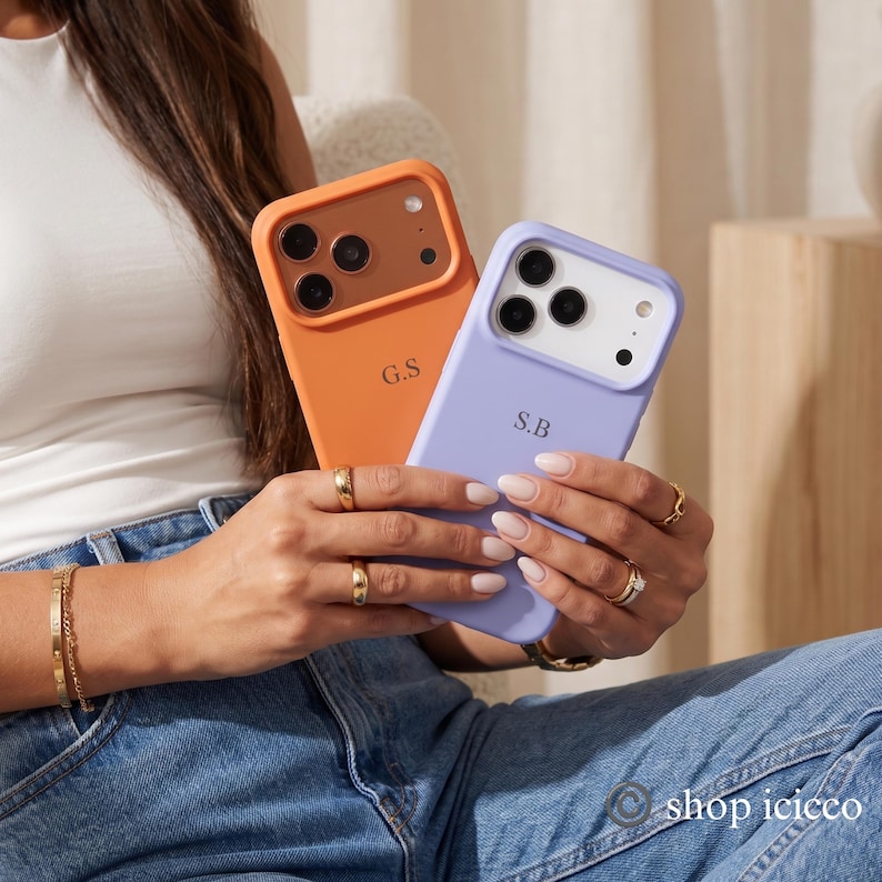 May include: Two silicone phone cases with camera cutouts. One case is orange with a brown camera frame and the initials G.S. The other case is light purple with a white camera frame and the initials S.B. Both cases feature a smooth matte finish.