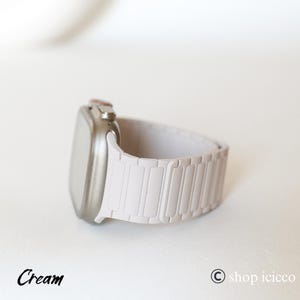 May include: Cream-colored smartwatch with a matching band. The watch has a rectangular screen and a metallic bezel. The band is made of rectangular links. The word "Cream" is written in cursive at the bottom left.