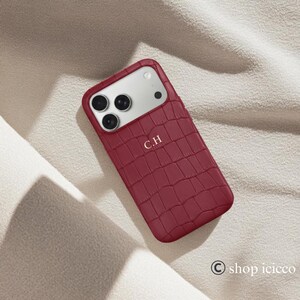 Puede incluir: Funda de tel&eacute;fono burdeos con textura de piel de cocodrilo. La funda tiene un recorte para la c&aacute;mara y las iniciales "C.H" est&aacute;n impresas en la parte delantera. La funda est&aacute; dise&ntilde;ada para un tel&eacute;fono inteligente.