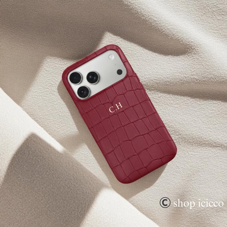 Puede incluir: Funda de tel&eacute;fono burdeos con textura de piel de cocodrilo. La funda tiene un recorte para la c&aacute;mara y las iniciales "C.H" est&aacute;n impresas en la parte delantera. La funda est&aacute; dise&ntilde;ada para un tel&eacute;fono inteligente.