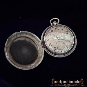 Peut inclure: Montre de poche argentée ouverte avec un cadran nacré, des chiffres et des aiguilles noirs. La montre est partiellement ouverte, révélant le mécanisme interne. Le texte "watch not included" est en bas.