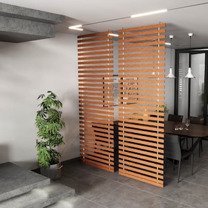 May include: A modern interior with a dining area and a wooden slat room divider. The divider is made of horizontal wooden slats. A dark wood dining table is surrounded by black chairs. A potted plant and a staircase are also visible.