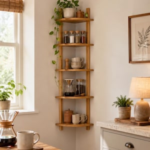 Wooden wall mounted corner shelf used as a kitchen coffee and spice rack, styled with glass jars, mugs, coffee accessories and indoor plants.