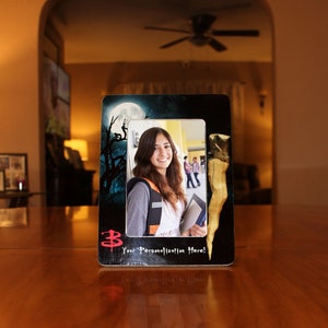 May include: A black picture frame with a dark background and a full moon. The frame has a white border and a red "3" symbol. The frame contains a photo of a young woman with long brown hair wearing a gray jacket and a white shirt. The photo also shows a group of people in the background. The text "Your Personalization Here!" is printed on the bottom of the frame.