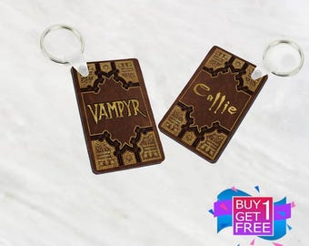 May include: Two brown wooden keychains with gold accents and intricate designs. One keychain says "Vampyr" and the other says "Callie".