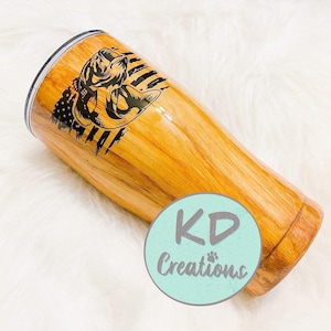 May include: A wooden-look tumbler with a black graphic of a fish and American flag design. The tumbler has a silver rim and a light blue circle with the text "KD Creations".