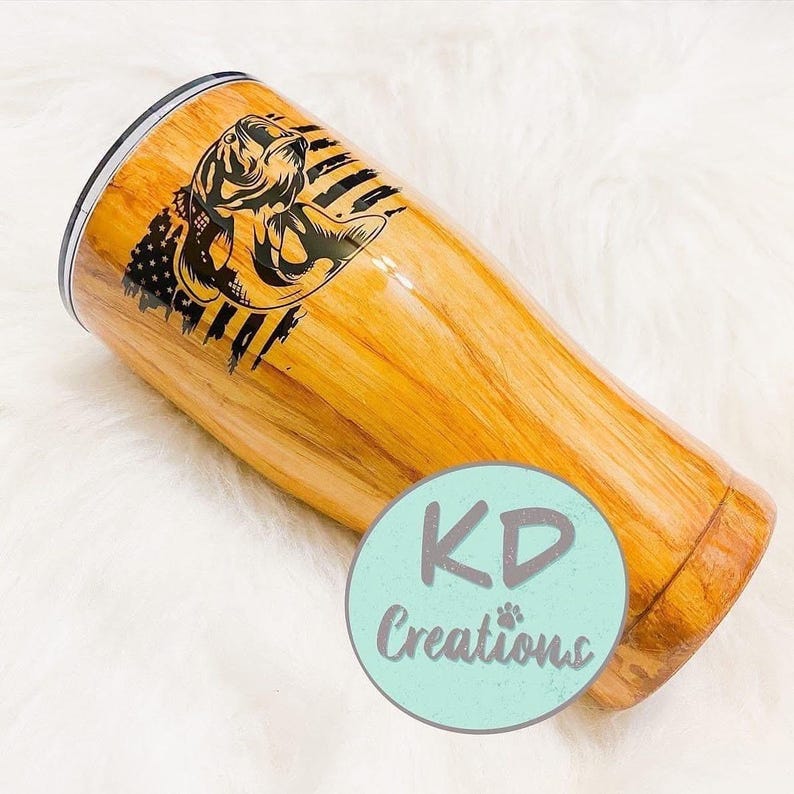 May include: A wooden-look tumbler with a black graphic of a fish and American flag design. The tumbler has a silver rim and a light blue circle with the text "KD Creations".
