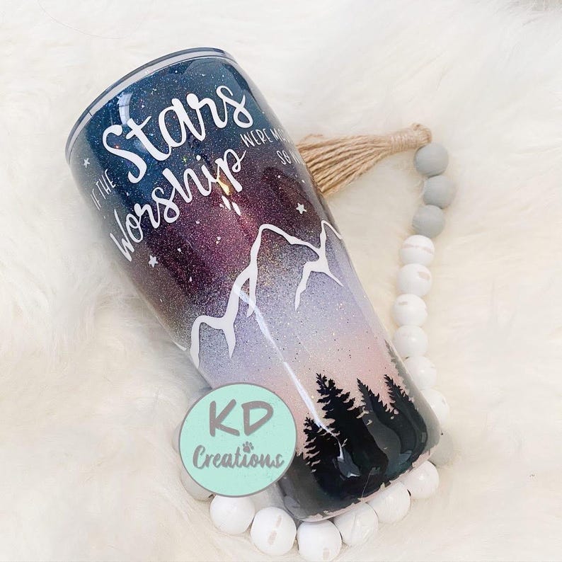 May include: A tumbler with a starry night design. The tumbler features the text "If the Stars Were Made to Worship" in white script. The design includes a mountain range and a forest silhouette. The tumbler has a glittery finish.