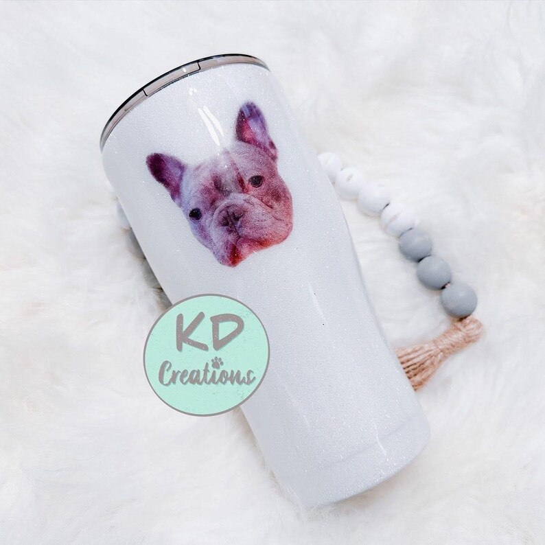May include: A white glitter tumbler featuring a French Bulldog portrait. The dog's face is a mix of pink and purple hues. The tumbler has a black lid and the text "KD Creations" in a circle.