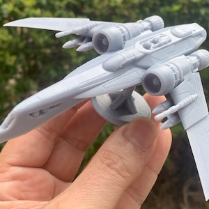 Pode incluir: Um modelo de nave espacial de pl&aacute;stico cinza com dois motores e uma cabine. O modelo est&aacute; em uma base circular.