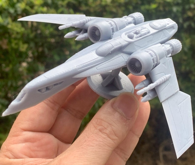 Pode incluir: Um modelo de nave espacial de pl&aacute;stico cinza com dois motores e uma cabine. O modelo est&aacute; em uma base circular.