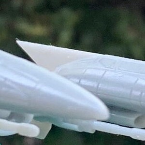 May include: Two white plastic model spaceships, one behind the other, with a slight angle to the left. The spaceship in the front is slightly larger than the one behind it.
