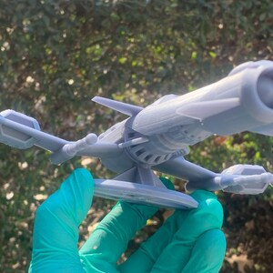 May include: A gray 3D printed model of a futuristic spaceship with a large engine and a small wing on the side. The spaceship is sitting on a circular base.