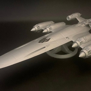 Op de afbeelding: Een grijs, gedetailleerd model van een futuristisch ruimteschip met meerdere motoren en een lang, slank lichaam. Het model staat op een witte standaard.