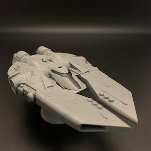 Może przedstawiać: Jasnoszary model statku kosmicznego o szczegółowym designie. Statek kosmiczny ma centralny korpus z dwoma rozłożonymi skrzydłami i wieloma elementami silnika. Model jest ustawiony na ciemnym tle.