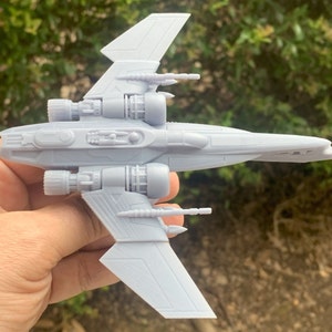 Pode incluir: Um modelo de nave espacial de pl&aacute;stico cinza com duas asas e v&aacute;rios motores. O modelo &eacute; detalhado com partes do motor e armas vis&iacute;veis.