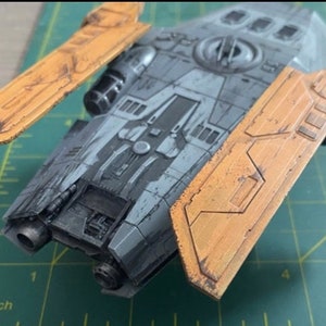 Peut inclure: Mod&egrave;le de vaisseau spatial gris et noir avec des ailes jaunes. Le mod&egrave;le est sur un tapis de coupe vert avec des marques en pouces.