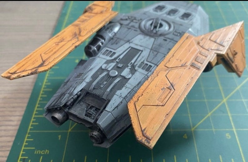 Peut inclure: Mod&egrave;le de vaisseau spatial gris et noir avec des ailes jaunes. Le mod&egrave;le est sur un tapis de coupe vert avec des marques en pouces.