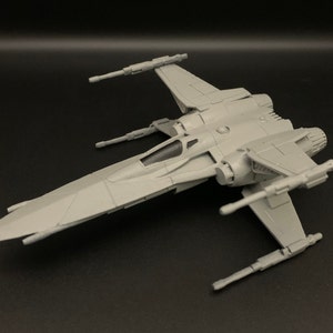 Puede incluir: Un modelo de plástico gris de un caza estelar X-wing de la franquicia Star Wars. El modelo está detallado con una cabina, alas y motores.