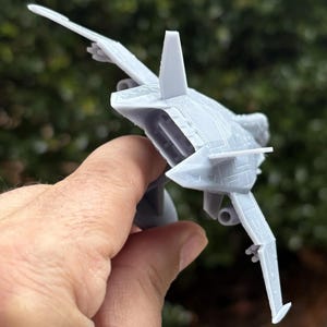 Puede incluir: Un modelo de avi&oacute;n gris claro con alas detalladas, un estabilizador vertical y un fuselaje elegante. El avi&oacute;n en miniatura se sostiene en una mano, mostrando su dise&ntilde;o y estructura. El modelo parece ser un avi&oacute;n de combate.