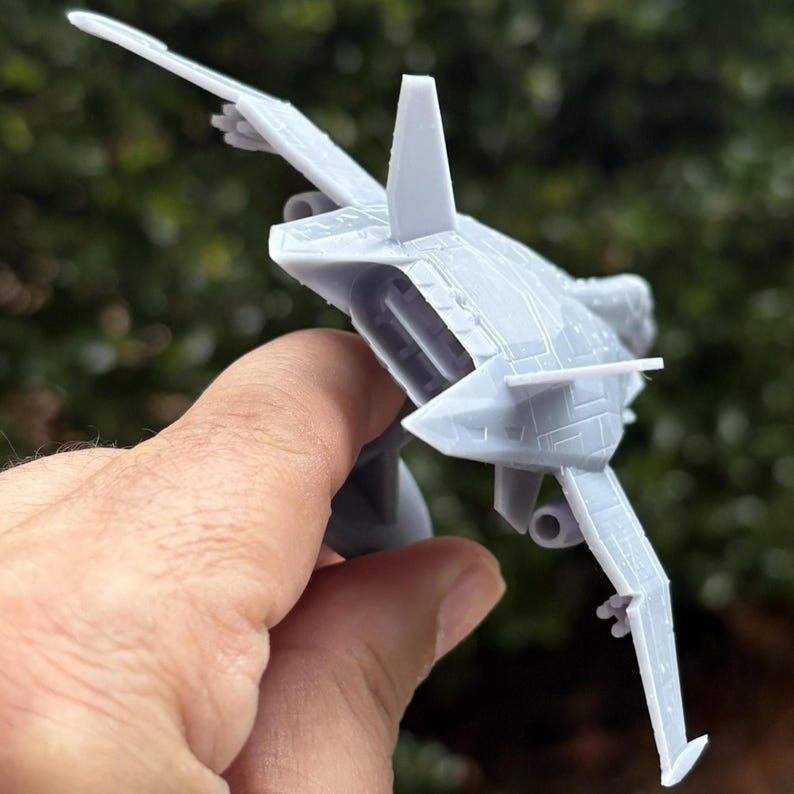 Puede incluir: Un modelo de avi&oacute;n gris claro con alas detalladas, un estabilizador vertical y un fuselaje elegante. El avi&oacute;n en miniatura se sostiene en una mano, mostrando su dise&ntilde;o y estructura. El modelo parece ser un avi&oacute;n de combate.