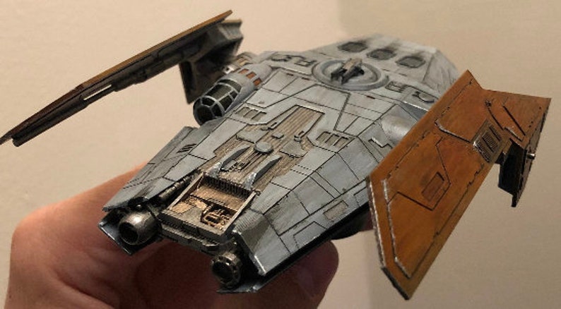 Peut inclure: Un mod&egrave;le d&eacute;taill&eacute; d'un vaisseau spatial avec un sch&eacute;ma de couleurs gris et brun. Le vaisseau spatial a un dessus plat et large avec un petit cockpit rond &agrave; l'avant. Le vaisseau spatial a deux ailes qui sont repli&eacute;es. Le mod&egrave;le est en plastique et mesure environ 25 cm de long.