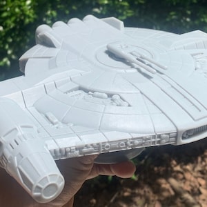 Puede incluir: Un modelo de nave espacial impreso en 3D blanco con una parte superior circular y un cuerpo largo y estrecho. La nave espacial tiene un diseño detallado con múltiples escotillas y compartimentos.