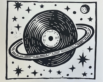 Può includere: Stampa linoleografica in bianco e nero raffigurante un disco in vinile a forma di pianeta, circondato da un anello, stelle e una luna. Il testo "ART IS HOW WE DECORATE SPACE" e "MUSIC IS HOW WE DECORATE TIME" è stampato sopra e sotto l'immagine centrale.