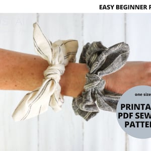 May include: Two fabric hair scrunchies, one white with black stripes and one gray with white stripes, are tied around a person's wrist. The text "one size PRINTABLE PDF SEWING PATTERN" is on a gray circle.