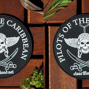 May include: Two black round patches with white text and graphics. The text reads "Pilots of the Caribbean" with a skull and crossbones graphic in the center. The website "clear2land.net" is printed at the bottom of each patch.