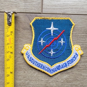 May include: A blue and yellow embroidered patch with the text "US SOUTHERN COMMAND AIR FORCES" and a radar symbol with a red lightning bolt.