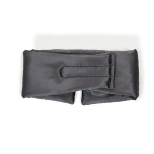 May include: A dark grey sleep mask made from a soft, silky fabric. The mask features a contoured design with a curved indentation for the nose and a strap that wraps around the head. Designed to block out light, it promotes better sleep.
