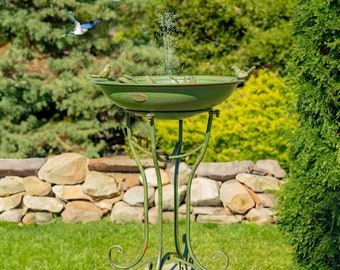 May include: A green metal bird bath with a fountain and a decorative stand. The bird bath is on a stone base and surrounded by green grass.