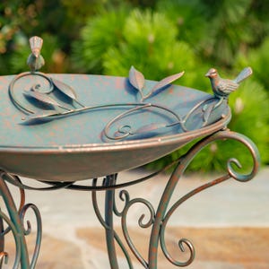 Puede incluir: Ba&ntilde;era para p&aacute;jaros de metal con acabado verde azulado y &oacute;xido. La base redonda est&aacute; adornada con hojas y vides, y dos figuras de p&aacute;jaros. La base tiene adornos decorativos. La ba&ntilde;era para p&aacute;jaros tiene un aspecto envejecido.