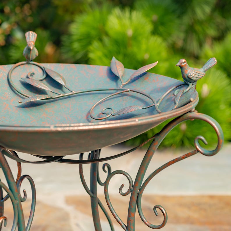 Puede incluir: Ba&ntilde;era para p&aacute;jaros de metal con acabado verde azulado y &oacute;xido. La base redonda est&aacute; adornada con hojas y vides, y dos figuras de p&aacute;jaros. La base tiene adornos decorativos. La ba&ntilde;era para p&aacute;jaros tiene un aspecto envejecido.