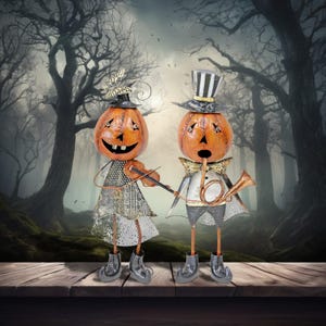 May include: Two Halloween-themed metal figurines with pumpkin heads, one playing a violin and the other a horn. They are dressed in festive attire, standing on a wooden surface against a spooky forest backdrop. The figurines have metal legs and feet.