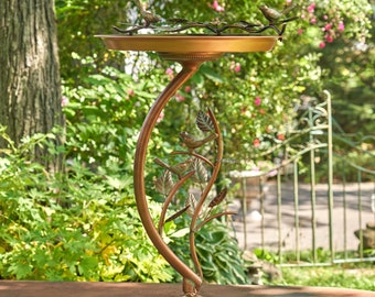 May include: A copper bird bath with a decorative stand featuring a stylized branch with leaves and birds. The stand has a curved design and three legs.