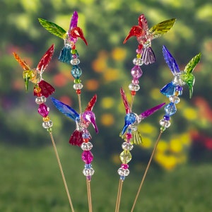 May include: A set of six colorful hummingbird garden stakes. Each stake features a hummingbird with iridescent wings and a beaded body. The hummingbirds are arranged in a cluster, with their beaks pointing in different directions.