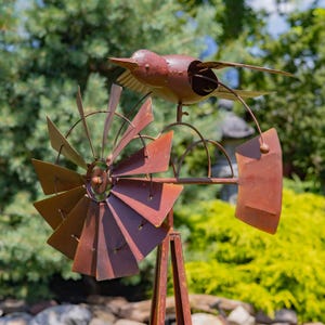 May include: A rustic metal bird weathervane with a windmill design. The bird is perched atop the windmill, with its wings outstretched. The windmill blades and frame have a weathered, reddish-brown finish, adding to the vintage aesthetic. Perfect for garden decor.