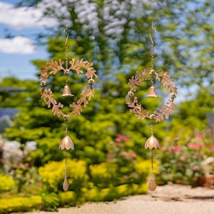 May include: Two gold heart-shaped wind chimes with bells hanging from the bottom. The chimes are made of metal and have a leafy design.