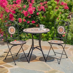 May include: A black metal patio set with a round mosaic tile table and two folding chairs. The chairs have a decorative metal back with a mosaic tile design.